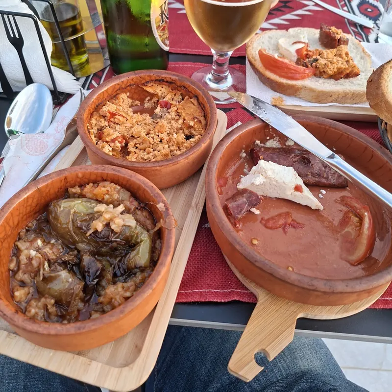 Stuffed peppers and other clay-pot dishes with a cold beer on a woven red placemat