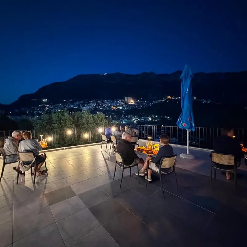 Guests dining on the terrace at night, the lights of Krujë on the hillside