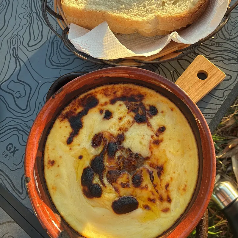 A golden baked dish in a clay pot next to a basket of fresh bread