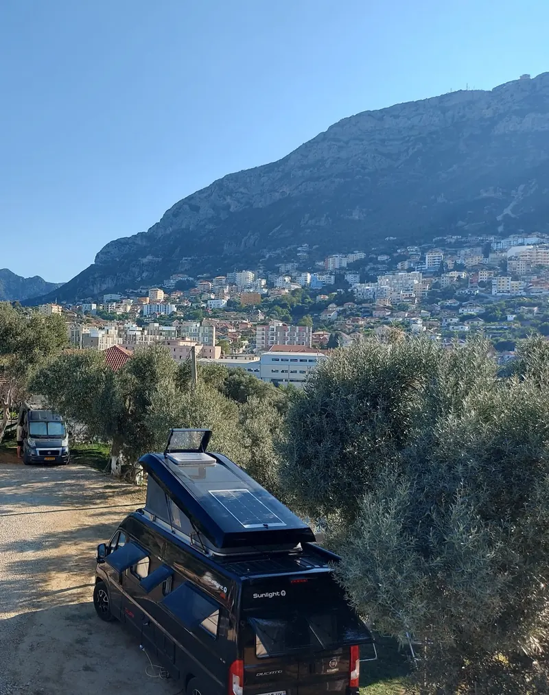 A camper van parked under olive trees, the town of Krujë and the mountain behind